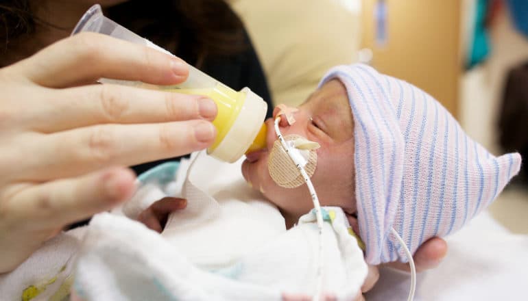 premature baby in hat drinks from bottle