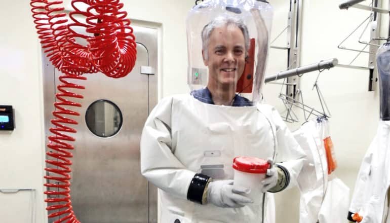 A researcher wears protective gear including a white body-suit with a clear plastic helmet