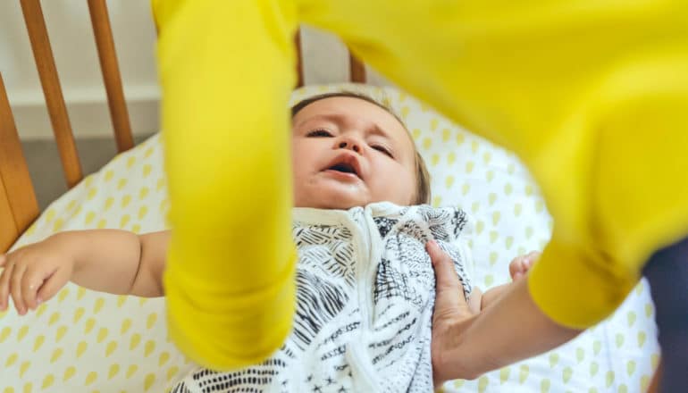 adult lowers crying baby into crib