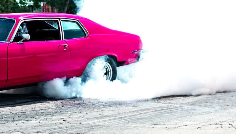 A pink muscle car burns out, smoke billowing from its back tires