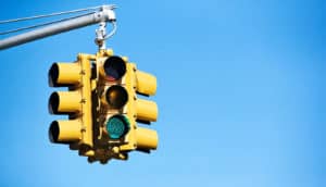 A yellow traffic light sits against a blue sky with its green light glowing