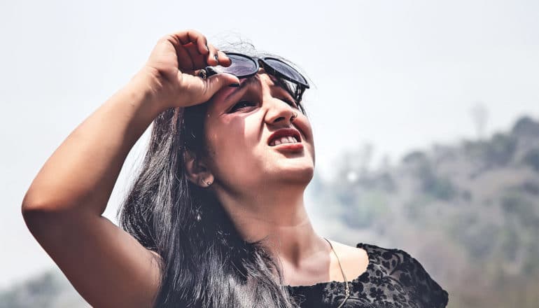 A woman grimaces as she raises her sunglasses off her eyes too look up at the sky