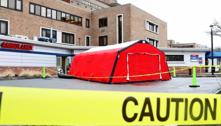 red tent outside hospital building, caution tape in foreground