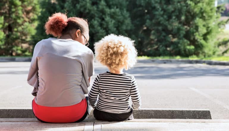 adult and child sit next to each on curb facing away