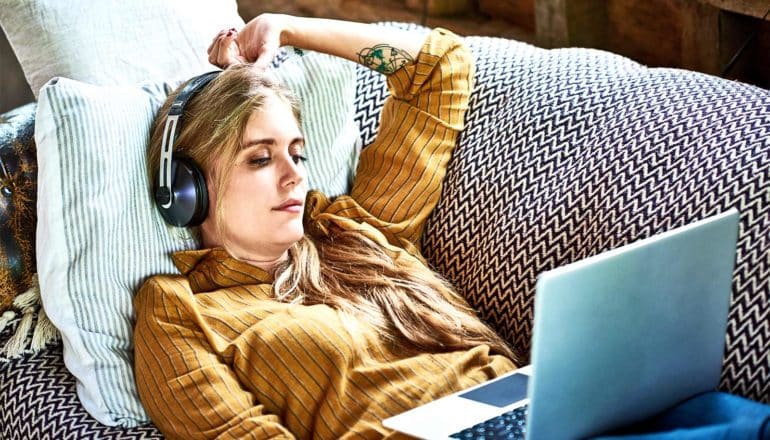 A young woman watches something on her laptop while laying on her couch