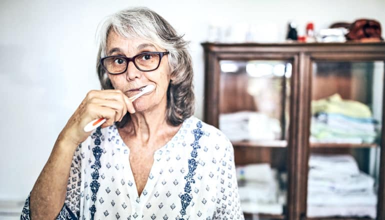 An older woman brushes her teeth