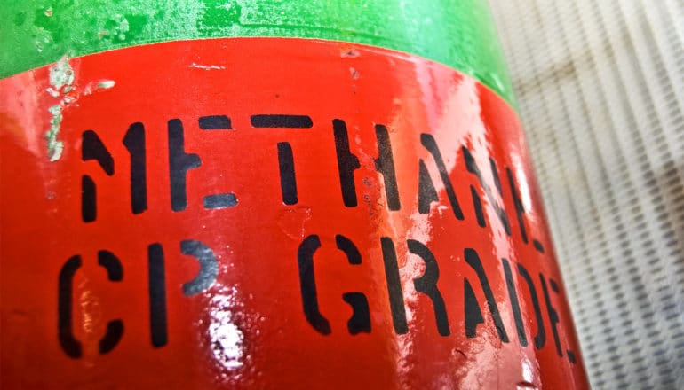 A green tank has a red label on it that reads "Methane CP Grade"