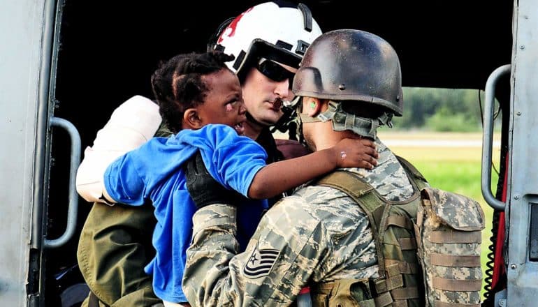 Harold takes a young boy in a blue shirt and a cast on his left arm from the arms of a soldier in fatigues