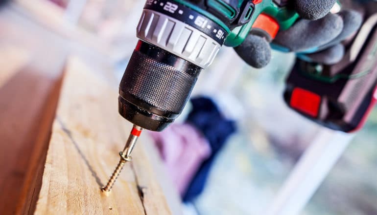 A person uses a drill to drive a screw into a board