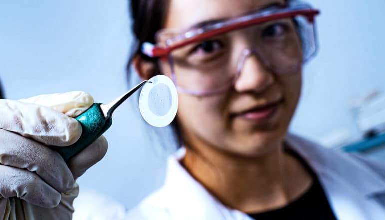 A researcher holds up a circle of filter paper with a pair of tweezers