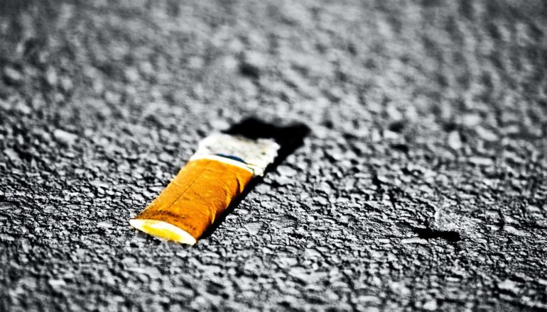 A cigarette butt sits crushed on asphalt