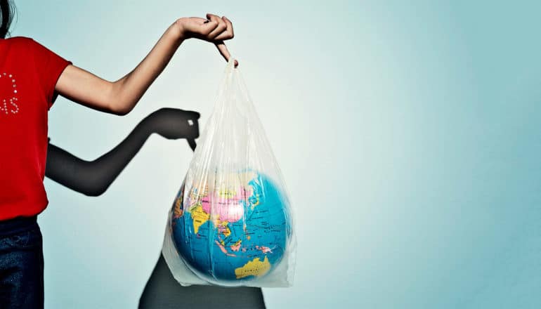 A woman in a red t-shirt holds up a plastic bag that contains a globe.