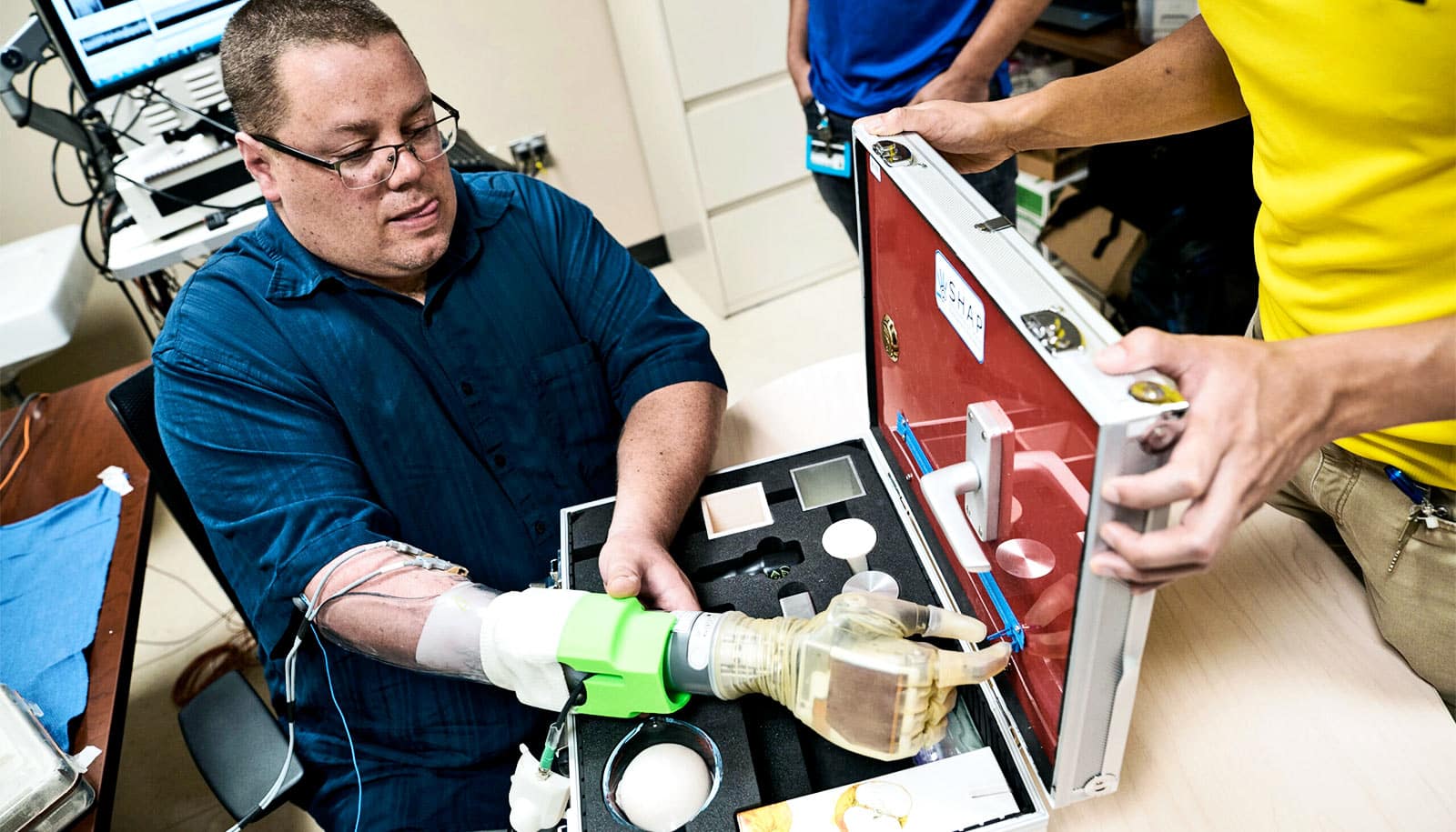 Hamilton uses the prosthetic arm to grab a small zipper in a suitcase of objects used to test the hand, holding it with his left hand and sticking his tongue out a bit with effort