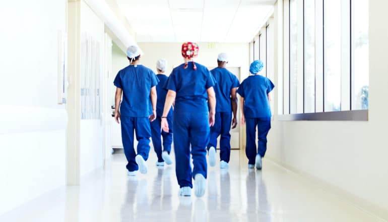 A group of surgeons in blue scrubs walk down the hall