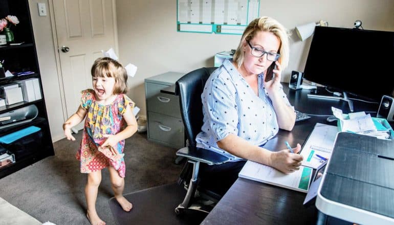 child jumps around behind adult working at desk in home office