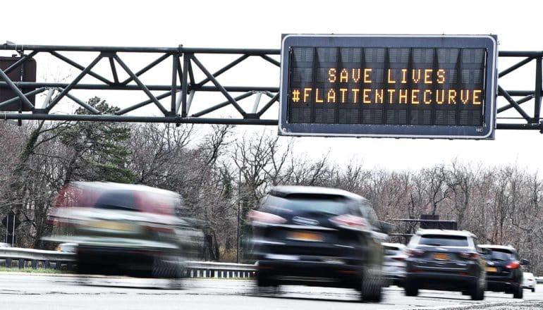Cars drive past a sign that reads "Save lives. Flatten the curve."
