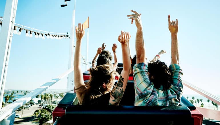 A couple put their hands up as they reach the top of a roller coaster