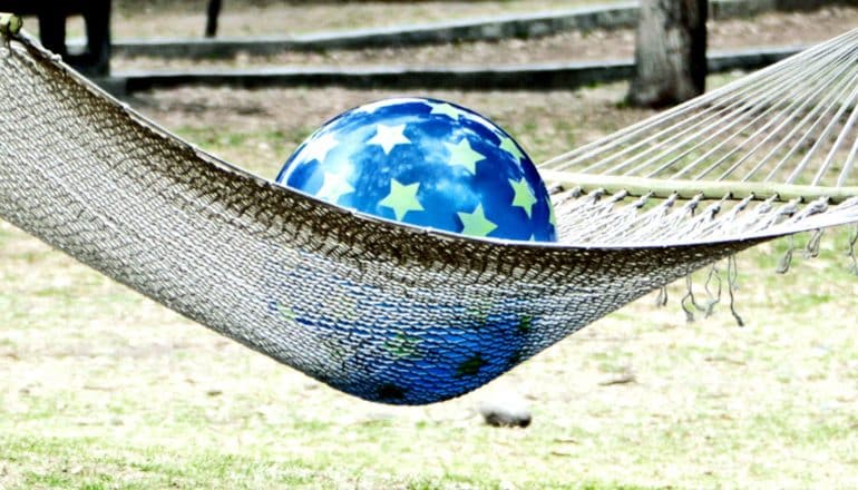 A blue ball covered in green stars sits on a hammock, with grass in the background