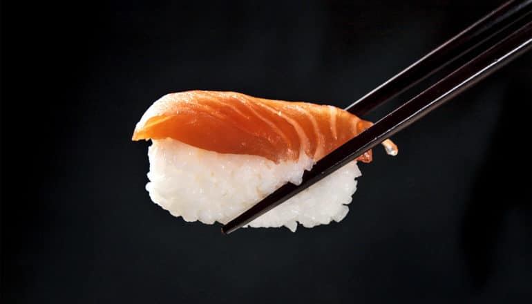 A pair of chopsticks hold a piece of salmon sushi