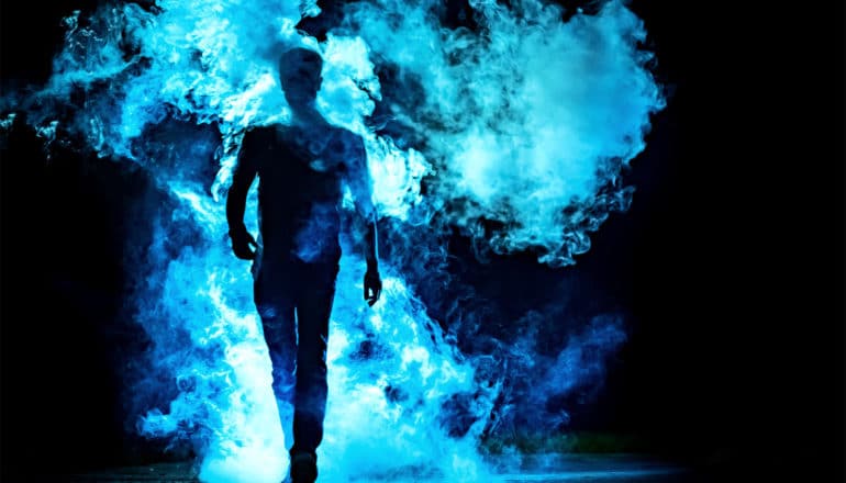 A man in silhouette walks through a cloud of blue smoke against a dark background