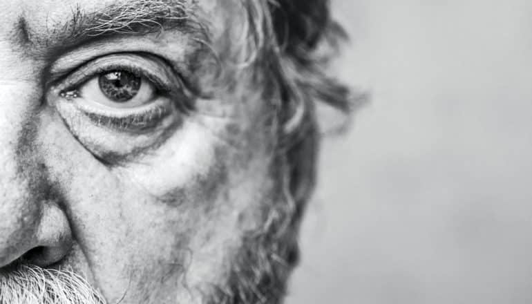 An older man stares into the camera in an extreme close-up only showing half of his face