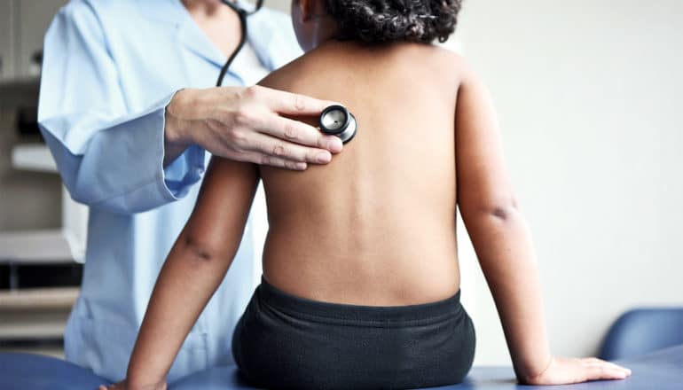 A doctor checks a young child's lungs with a stethoscope