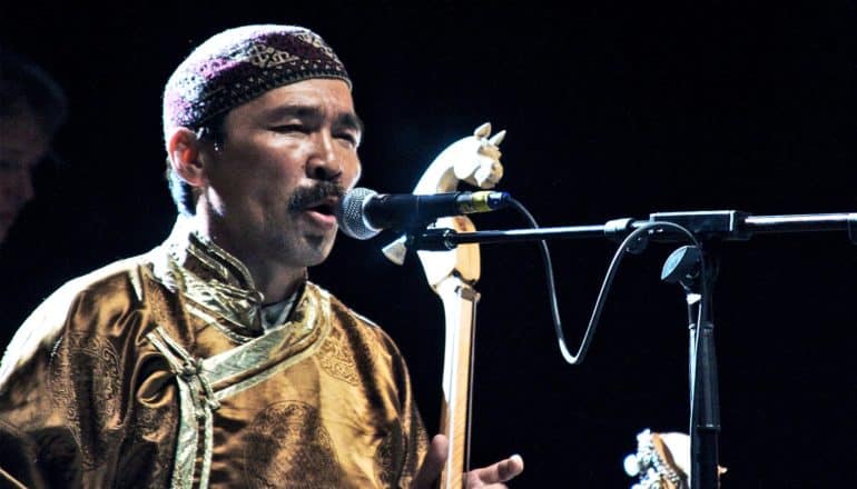 A man plays a stringed instrument with a horse head at its top while singing on stage