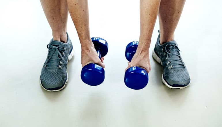 A person picks up blue weights, with just their arms and legs visible against a white background