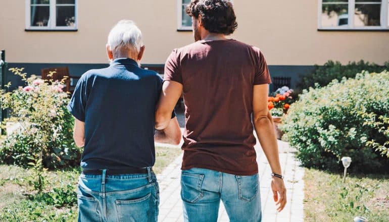 rear view of elderly and younger person walking outdoors with linked arms