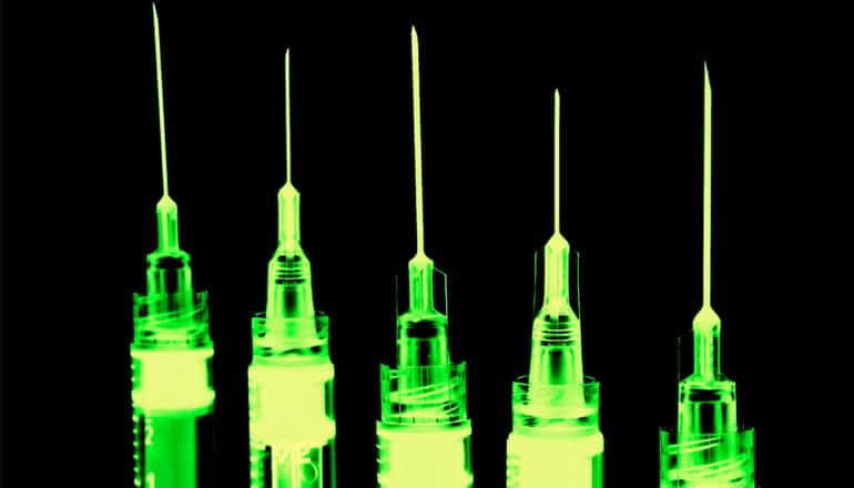 Five syringes glow green against a black background