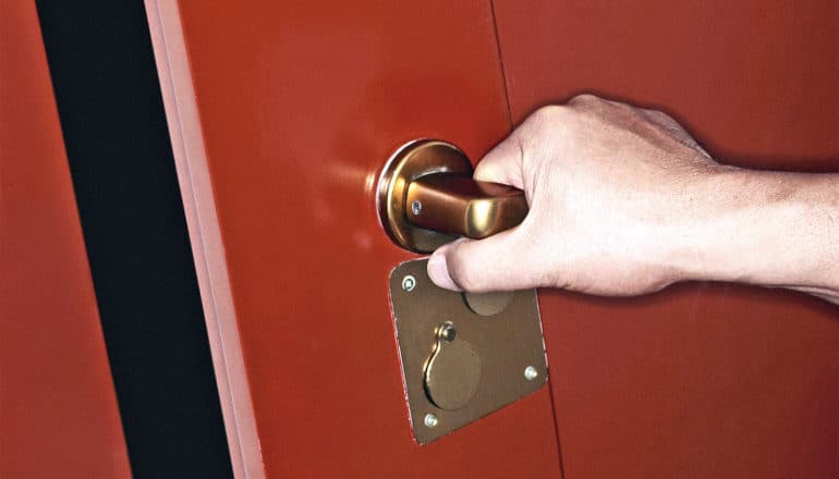 A person opens a red door with gold metal handle