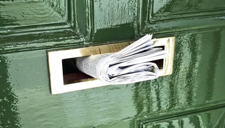 A newspaper sits in a green door's mail slot