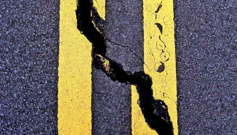 A road with two solid yellow stripes is cracked diagonally down its center