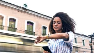 A young woman in a blue striped shirt looks at her watch