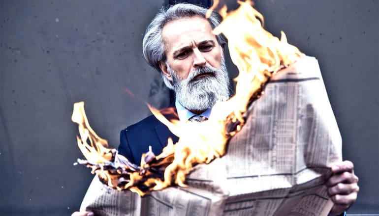 A man in a suit reads a newspaper that's on fire