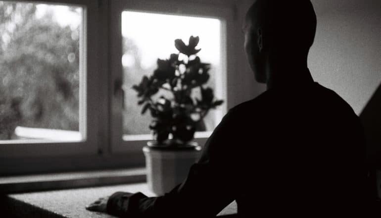 b/w image: person in silhouette sits before window
