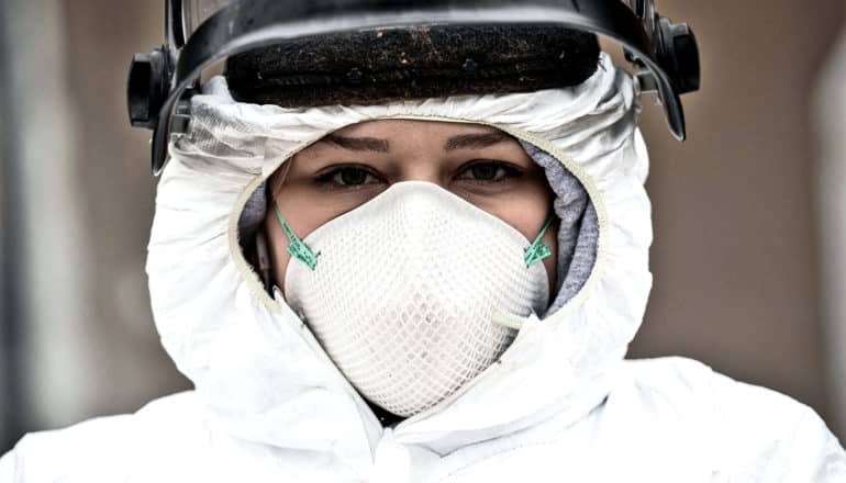 A nurse wears a white mask and white body suit