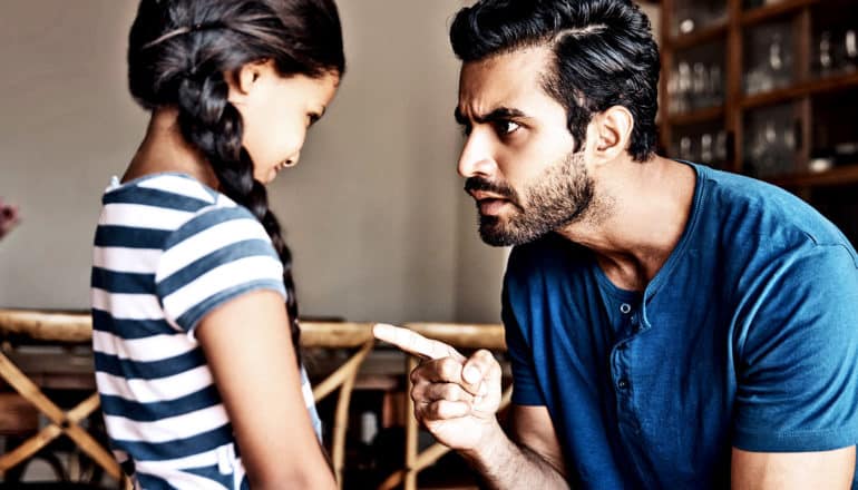 A father in a blue shirt leans down and chastises his daughter, whose wearing a striped shirt