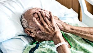 An older hospital patient touches his face while in bed