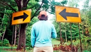 A man stands between two yellow signs pointing in different directions