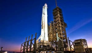 A SpaceX rocket stands ready for lift-off against a deep blue sky at dusk