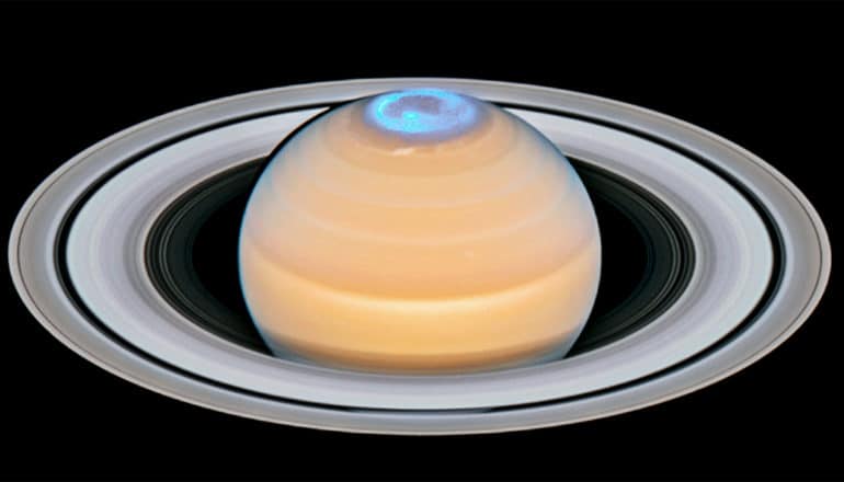 Saturn looks orange and its ring looks gray against the blackness of space. At the top of the planet, its aurora is highlighted in blue