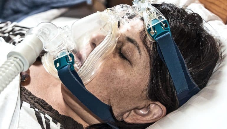 A woman has a sleep apnea mask over her face as she sleeps