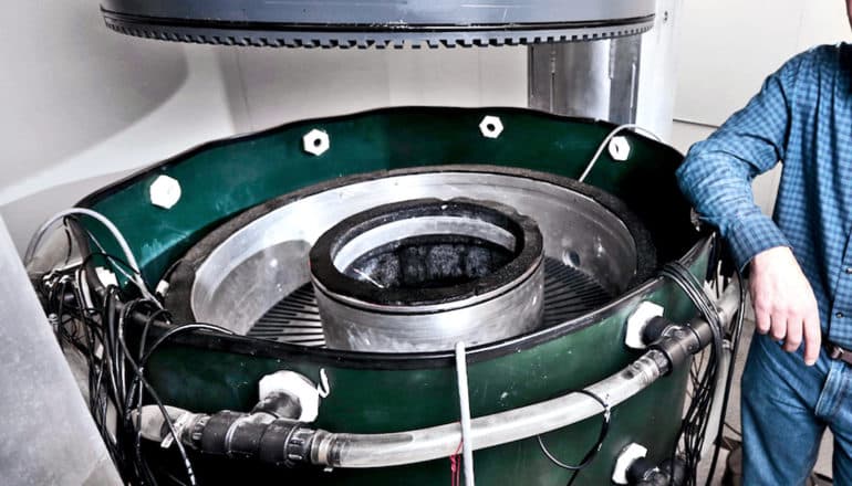 A researcher leans on the 9-foot tall machine, which is a circular drum that looks slightly like a turbine