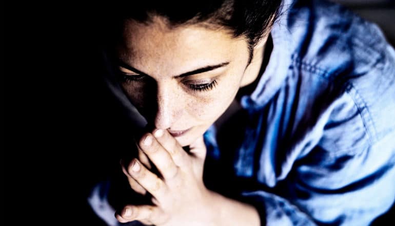 A young woman looks concerned as she touches her hands to her face