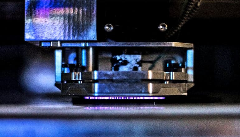 Purple light illuminates a close up of a piece of a 3D printer