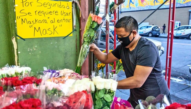 A man with a mask on restocks flowers at a flower shop with a sign requiring customers to wear masks