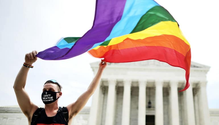 A person holds a rainbow flag in front of the Supreme Court