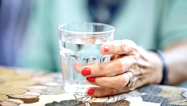 hand with red nails and ring holds glass of water