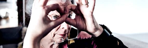 An older woman looks at the camera through her hands, shaped like glasses